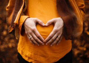 Hands making a heart over a Mom's tummy that is pregnant