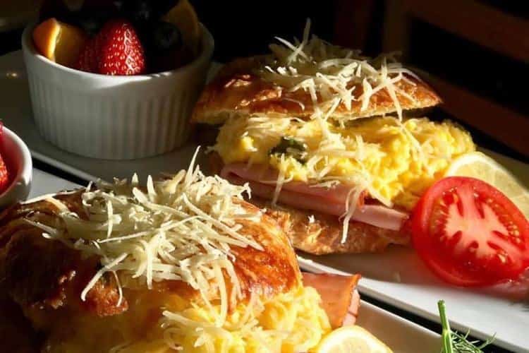 Cheese topped baked dishes next to sliced tomatoes and fresh fruit