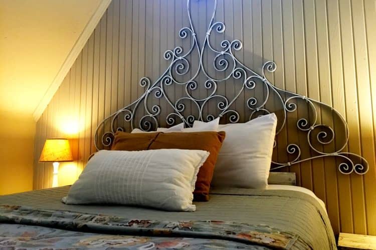 Guest bed with scrolling iron headboard, nightstands with lamps and sloped ceiling