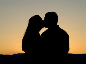 Silhouelle of a couple kissing with the sunset behind them.