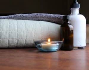 Folded white blanket and towel next to a burning tea light candle and two bottles