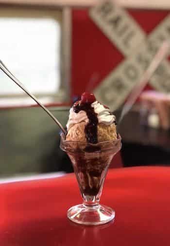 Glass dessert dish filled with ice cream, chocolate syrup and a red cherry on top