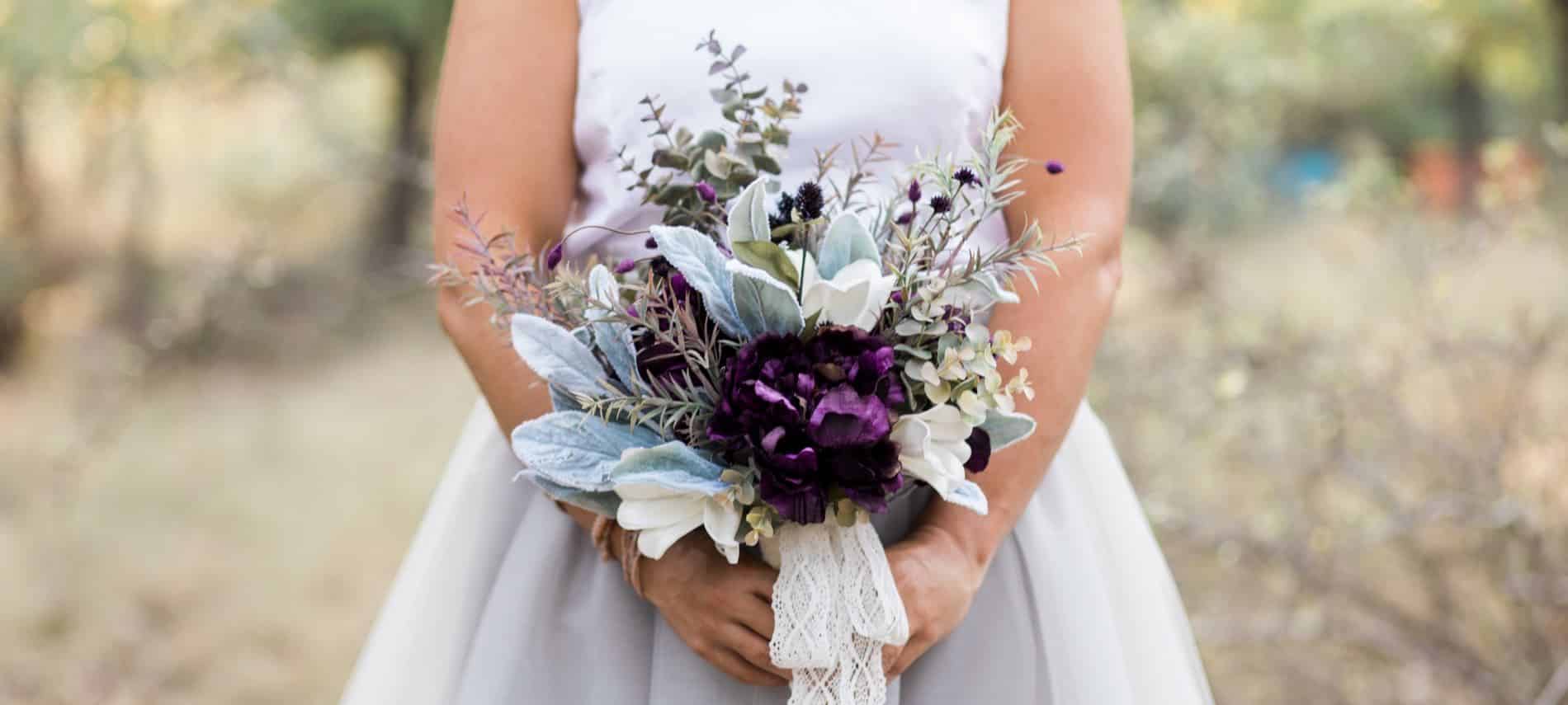 Partial view of a bride in white holding a white and burgundy floral bouquet